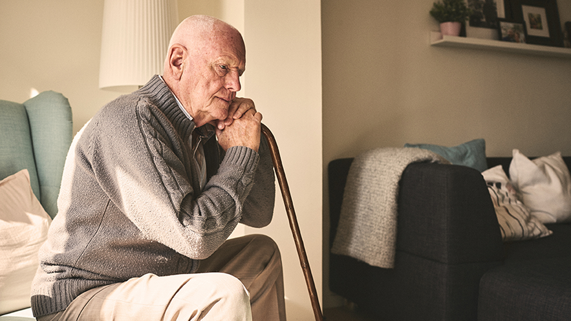 Elderly man sitting alone at home Thoughtful elderly man sitting alone at home with his walking cane